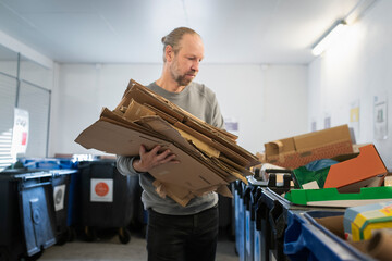 Mature man collecting cardboard boxes while standing near disposal containers