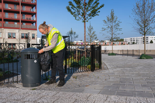 Sanitation worker in reflective clothing throwing garbage bag in bin at street