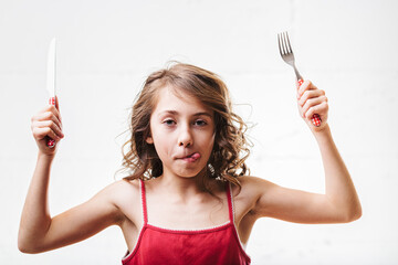 Playful child holding fork and knife with anticipation