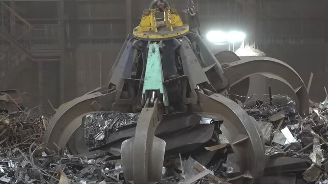 Modern industrial recycling facility featuring overhead grapple cranes sorting scrap materials with massive circular container demonstrating advanced waste management operations.