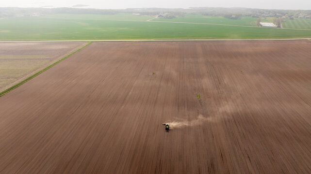 Aerial view of tractor plowing agricultural field at foggy day