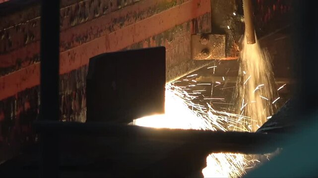 Witness the intense process of hot steel billets being transported on a conveyor in a steel mill. The glowing metal highlights the industrial operation.