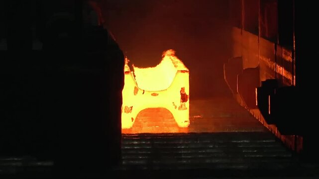 Witness the intense process of hot steel billets being transported on a conveyor in a steel mill. The glowing metal highlights the industrial operation.