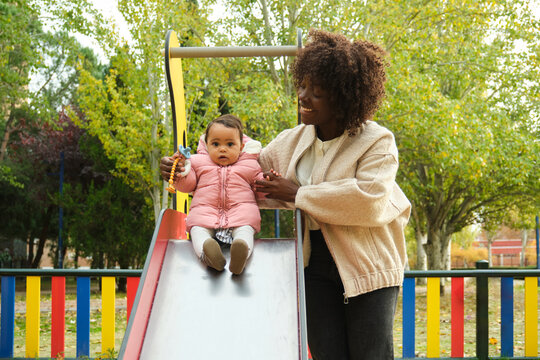 Mother helping her baby daughter going down a slide at the playground