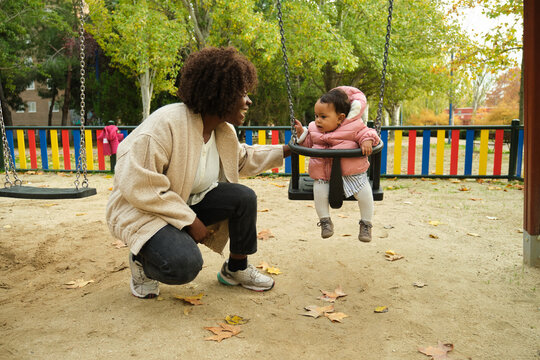 Mother pushing her baby daughter on a swing in a playground