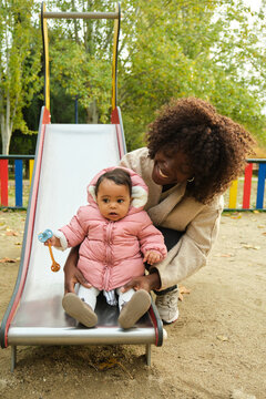 Happy mother helping her baby daughter going down the slide