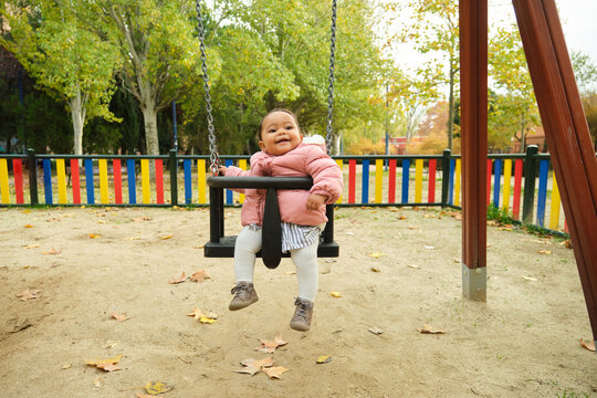 Happy baby girl having fun swinging at playground in autumn
