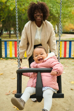 Happy baby girl swinging at playground with mother pushing