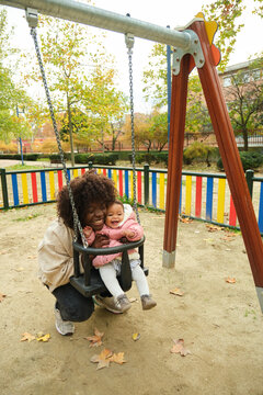 Mother pushing her laughing baby daughter on a swing in a playground