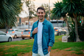 Young man smiles in a park while casually dressed during sunset