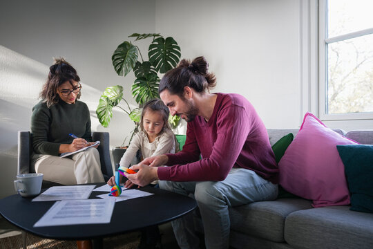 Father and daughter playing with fidget toy in front of psychotherapist during therapy session