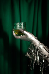 Person with Silver Glove Holds Whisky Glass Against Green Backdrop