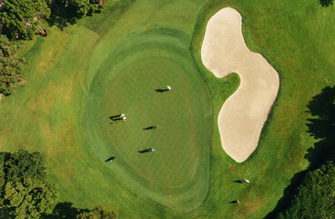 Aerial drone shot of a golf course with golfers on green grass near a sand bunker