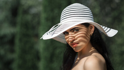 The woman looks at the camera with a slight smile.  The light falls in such a way that the stripes from the hat create shadows on her face.