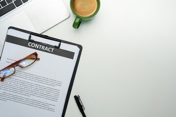 Close up of contract on clipboard, glasses, a cup of coffee and laptop on organized workspace