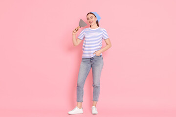 Young decorator with putty knife on pink background