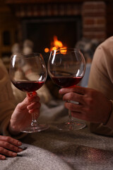 Couple with glasses of red wine near burning fireplace, closeup