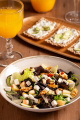 A fresh salad with feta, walnuts, apples, and crackers with cucumber and tsasiki, accompanied by orange juice