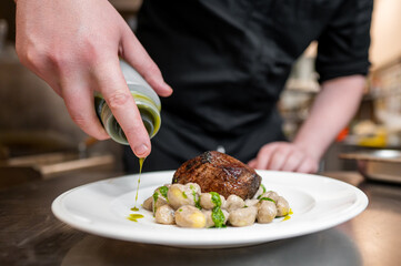 A chef drizzles olive oil over a gourmet dish featuring a perfectly cooked piece of meat on a bed of gnocchi, garnished with fresh herbs. Captures the art of culinary presentation.