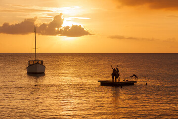 Group of young locals jumping into Caribbean Sea from pontoon off the beach of Boka Sint Michiel, Curacao, in sunset