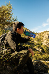 Vertical image of young hiker on top of a mountain sitting drinking water from a bottle on a sunny day