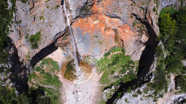 Majestic rinka waterfall flows down rocky cliffs in logarska dolina valley, creating a picturesque scene amidst lush greenery under a vibrant blue sky