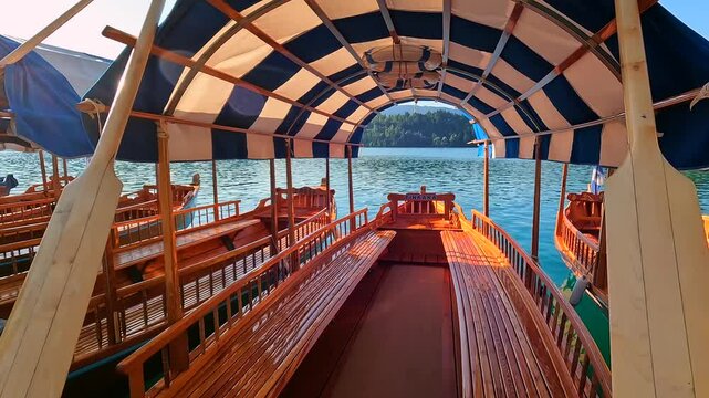 Wooden tourist boats moored at dock on lake bled in slovenia with bled island and iconic church in background and sun shining through canopy