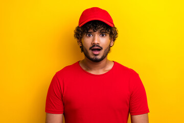 Young man in bright red casual attire surprised against vibrant yellow wall.