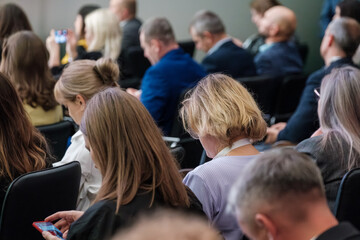 People attending a conference sitting in rows, deeply engaged, with one person using a phone. Atmosphere of concentration and professional interest.