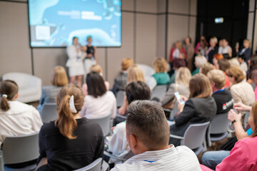 Attendees engaging in a business presentation featuring speakers in a professional conference setting. Modern venue emphasizes collaboration and knowledge sharing among participants.