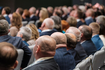 Large audience attentively participating in a corporate meeting or presentation indoors, suited professionals and seating arrangement.