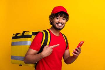 Cheerful young delivery man in casual attire using a smartphone against a vibrant yellow background