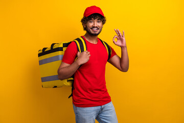 Portrait of a cheerful deliveryman in a red t-shirt and cap with a yellow backpack against a vibrant yellow background