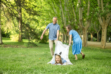 Obraz premium Parents playing with daughter in park, pulling blanket tunnel