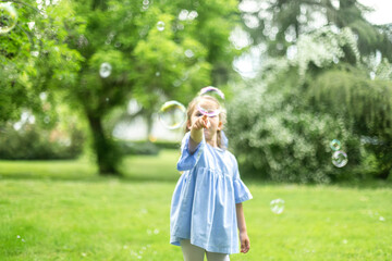 Little girl playing with soap bubbles in a green park