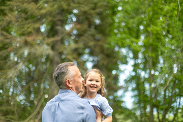 Father holding his smiling daughter in a green park