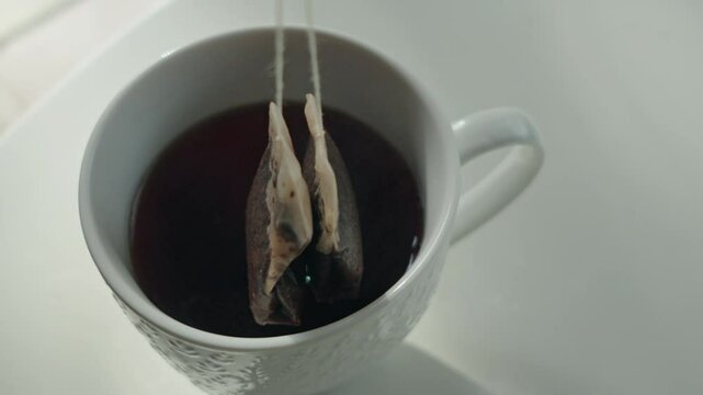 Closeup of moving tea bags out of water in white mug on the table
