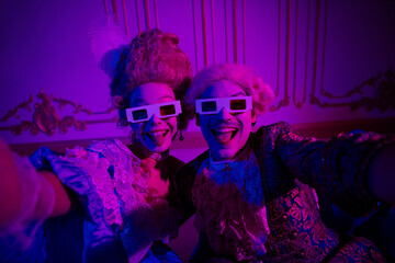 Joyful couple in vintage costumes enjoying a fun moment in a neon-lit baroque setting with...