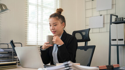 Fototapeta premium Businesswoman sitting at desk on couch in workplace or at home working on laptop and analyzing data on charts and graphs and writing on papers to make business plan and strategies for company, 