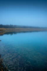 Autumn morning on the blu lake with fog , reflections on water ,landscape photography .Blue colors ,blue water ,mystery weather on the ponf.Forest near the pond , morning landscape at autumn season