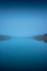 Autumn morning on the blu lake with fog , reflections on water ,landscape photography .Blue colors ,blue water ,mystery weather on the ponf.Forest near the pond , morning landscape at autumn season