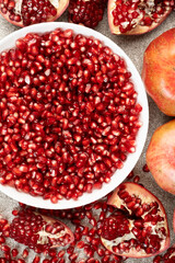 Pomegranate seeds in a plate and lots of whole and peeled pomegranates.