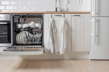 Built-in dishwasher full of clean dishes with its door open, white utensil. Modern technologies in...