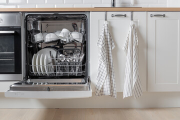 Built-in dishwasher full of clean dishes with its door open, white utensil. Modern technologies in...