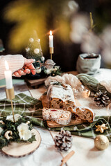 Woman dusting stollen with powdered sugar on a festive table, Scandinavian style, Scandinavian Christmas, stollen with powdered sugar, raisins, candied fruits
