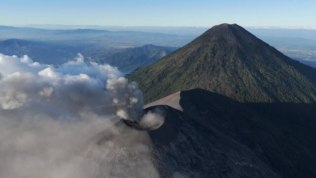 Aerial view of Volcan de Fuego emitting thick smoke with lush green slopes and a vast Guatemalan landscape in the background