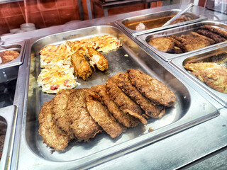 A variety of freshly cooked fried cutlets and omelets displayed in a bustling eatery during...
