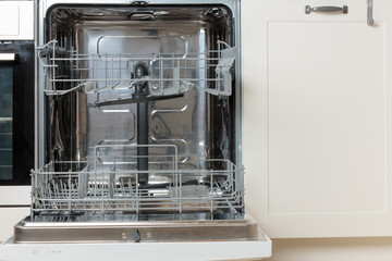 Built-in empty dishwasher with its door open. Modern technologies in the home kitchen with minimalistic white cabinetry. Simplifying daily housework.