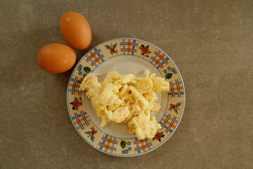 A colorful plate of freshly prepared scrambled eggs, accompanied by two whole brown eggs on a kitchen countertop.