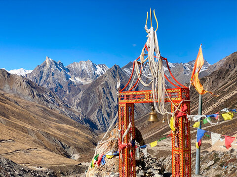 Sacred gate with flags and temple bell on the road leading to Om Parvat. Sheshnag Parvat, a snake-shaped mountain, in the background
